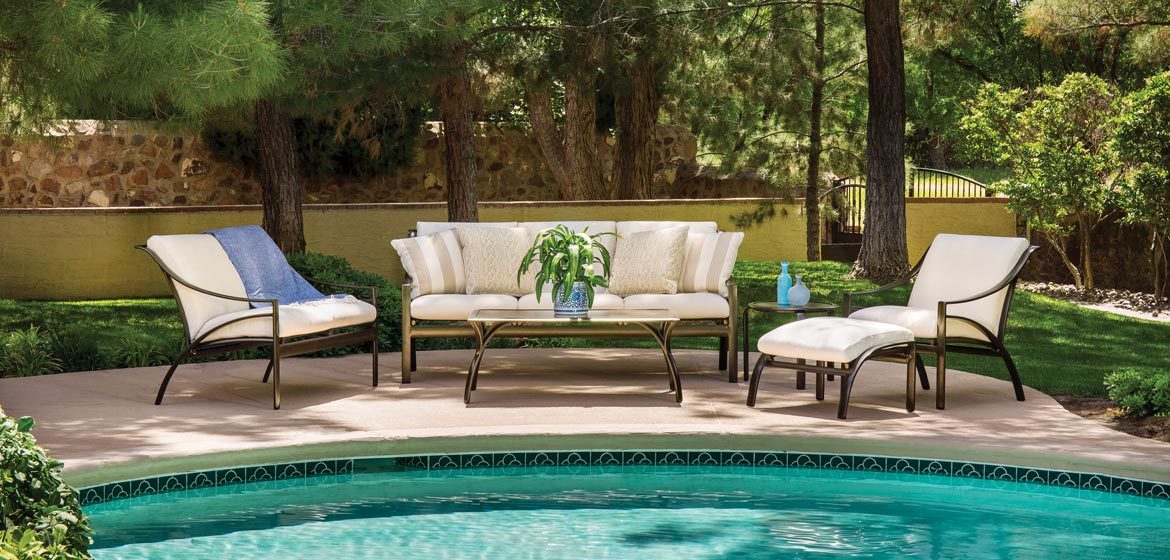 Pasadena outdoor cushion seating from brown jordan with sofa, lounge chair, ottoman and coffee table on a pool deck in the woods with a beautiful stone wall in the background