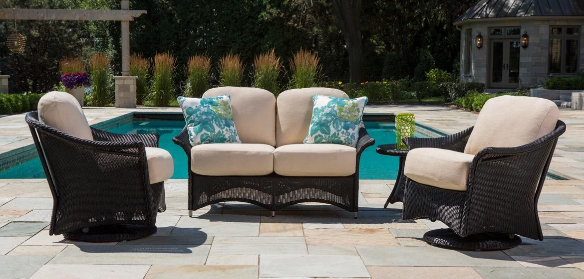 Lloyd Flanders Generations outdoor wicker cushion seating with love seat and swivel glider chairs on flagstone patio by a beautiful pool and pergola